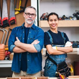 một người đàn ông và một người phụ nữ trung niên mặc đồng phục lao động bằng vải denim đứng trước các giá trưng bày dụng cụ cầm tay